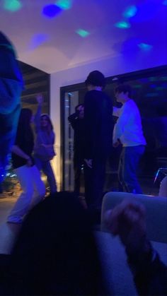 a group of people standing around in a living room with blue lights on the ceiling