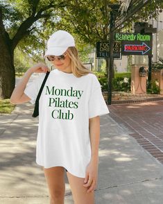 a woman is standing on the sidewalk wearing a shirt that says monday pilates club