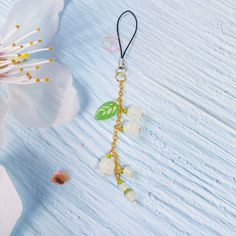 a white flower with green leaves and beads hanging from it's side on a black cord