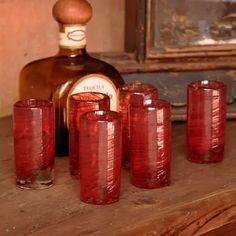 a bottle and five red glasses on a table