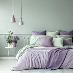 a bed with purple and green pillows in a bedroom next to a table filled with flowers