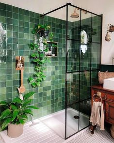 a bathroom with green tiles and a plant in the corner, next to a shower stall