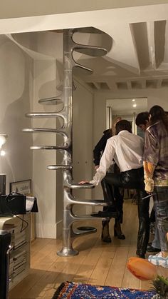 several people standing in a living room near a spiral metal object on the wall and floor