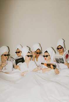 five women in white robes and sunglasses are sitting on a bed