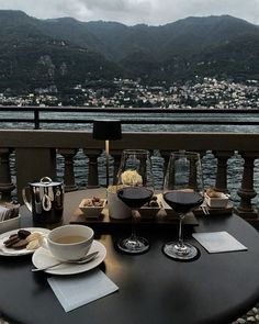 a table with two glasses of wine and plates of food on it overlooking the water