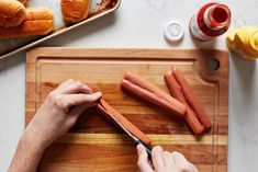 a person cutting up carrots on top of a wooden cutting board next to buns