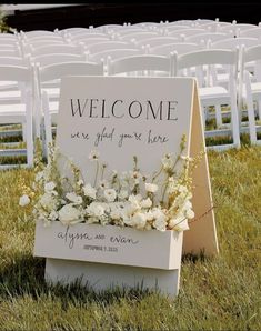 a welcome sign sitting on top of a grass covered field next to rows of white chairs