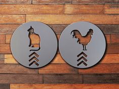 two circular metal signs with roosters on them against a wooden wall in the shape of circles