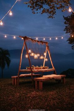 a wooden table with lights hanging from it and some benches under the tree in front of it