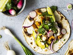 two tacos with meat, onions and cilantro on a blue surface next to other vegetables