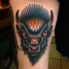 a bison tattoo on the leg of a man with red eyes and an orange eye