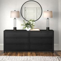 a black dresser with two lamps and a round mirror