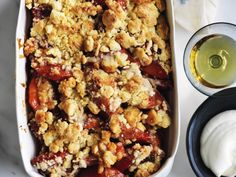 a casserole dish filled with fruit and crumbs next to a glass of white wine