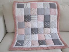 a white couch with a pink and gray patchwork quilt on it's back