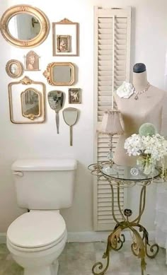 a white toilet sitting in a bathroom next to a table with flowers and mirrors on it