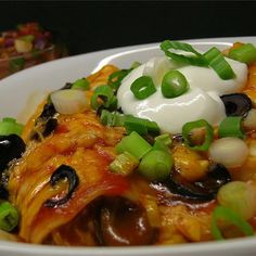 a white bowl filled with pasta covered in cheese and green onions, topped with sour cream