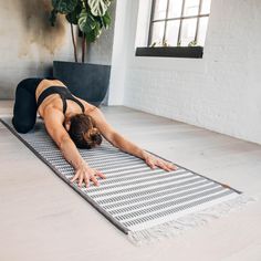 a woman is doing yoga on a mat in the middle of a room with a potted plant