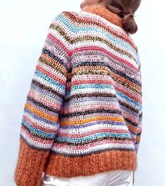 a woman wearing a multicolored sweater and white pants with her hair in a pony tail