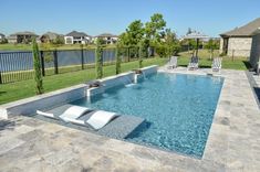 a swimming pool surrounded by lawn chairs and fenced in area with grass, trees, and houses