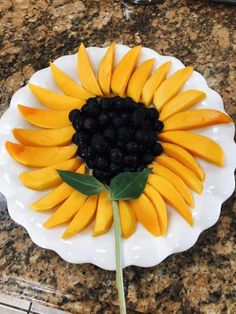 a white plate topped with sliced fruit and a sunflower on top of a counter