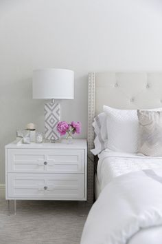 a bedroom with white furniture and pink flowers on the nightstand