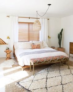 a bedroom with a bed, rugs and plants in the corner on the floor