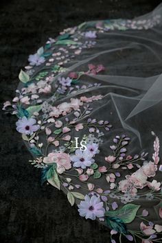 a veil with flowers on it is laying on the ground next to a black background