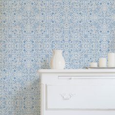 a white dresser sitting next to a wall with blue and white flowers painted on it