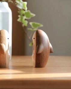 two wooden elephants sitting next to each other on top of a table in front of a vase