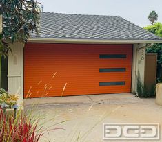 an orange garage door is open in front of a house with trees and bushes around it