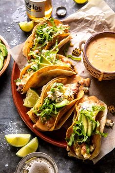 several tacos on a plate next to a bowl of soup and some limes