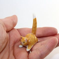 a hand holding a tiny toy cat in it's palm with white and yellow tail