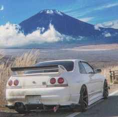 a white car is parked on the side of the road in front of a mountain