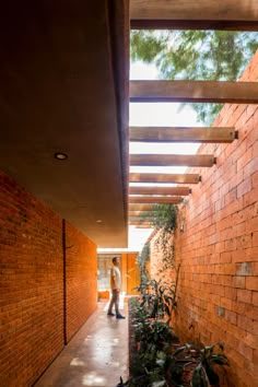 a man walking down a hallway between two brick buildings with plants growing on the side