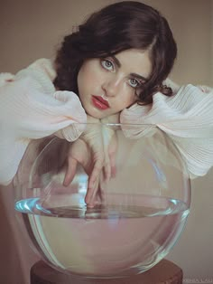 a woman with her hands on the top of a fish bowl, looking at the camera