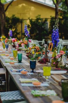 a long wooden table topped with lots of vases filled with colorful flowers and greenery