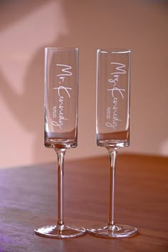 two wine glasses sitting on top of a wooden table next to each other with writing on them