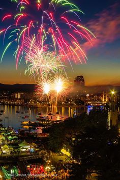 fireworks are lit up in the night sky over a harbor and cityscape with boats on it