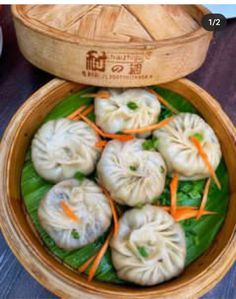 a wooden bowl filled with dumplings on top of a green leaf covered table next to a bamboo basket