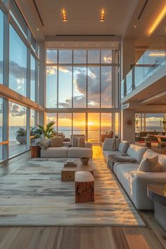 a living room filled with lots of furniture next to large windows overlooking the ocean at sunset