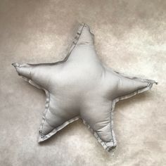 a white star shaped pillow sitting on top of a gray surface with no one around it