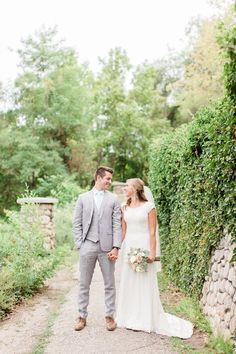 a bride and groom walking down a path in front of some bushes at their wedding