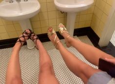 two women's legs with sandals on in a bathroom