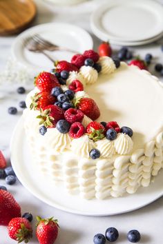 a white cake with berries and blueberries on it sitting on a table next to plates