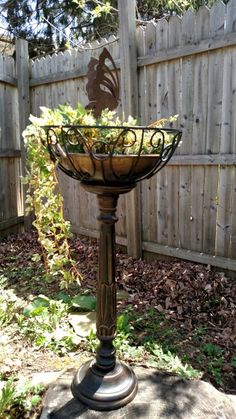 a metal basket with plants in it sitting on top of a stone slab next to a fence