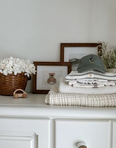 a white dresser topped with lots of folded clothes and framed pictures on top of it