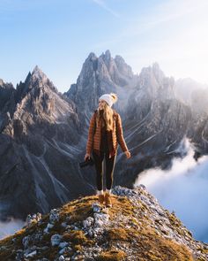 a woman standing on top of a mountain with a camera in her hand and looking at the mountains