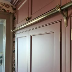 a close up of a door handle on the side of a pink kitchen cabinet with floral wallpaper