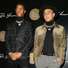 two men standing next to each other in front of a black wall with writing on it