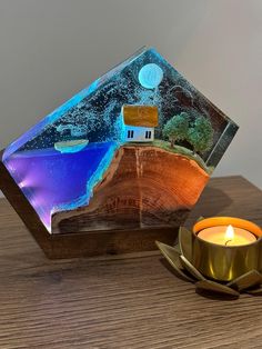 a candle sitting on top of a wooden table next to a glass block with a house in it